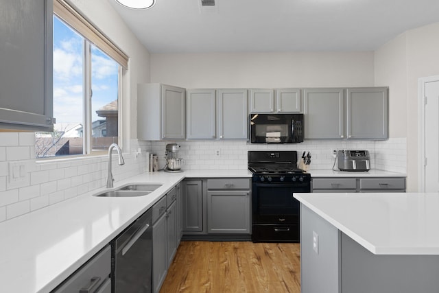 kitchen with light wood-type flooring, black appliances, gray cabinets, and a sink