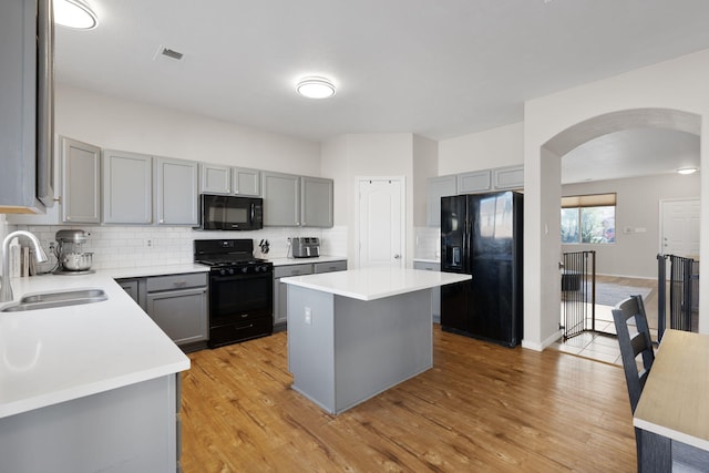 kitchen with black appliances, a kitchen island, a sink, and gray cabinetry