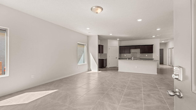 unfurnished living room with light tile patterned floors, a textured ceiling, baseboards, and recessed lighting