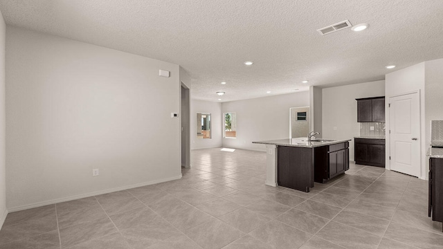 kitchen with a kitchen island with sink, a sink, visible vents, open floor plan, and backsplash