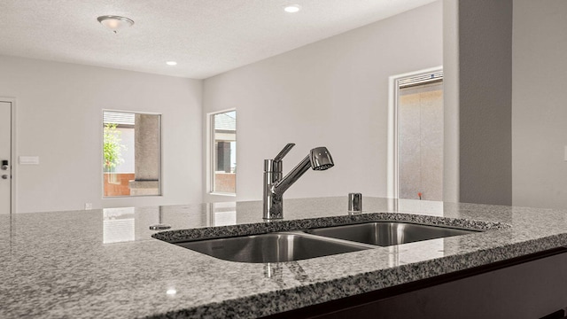 kitchen featuring stone countertops, recessed lighting, a sink, and a textured ceiling