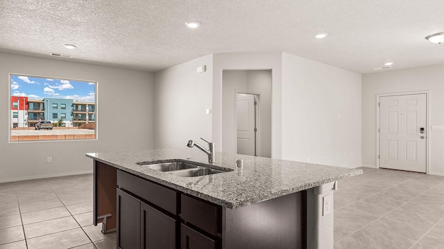 kitchen featuring light tile patterned floors, light stone counters, a sink, visible vents, and an island with sink