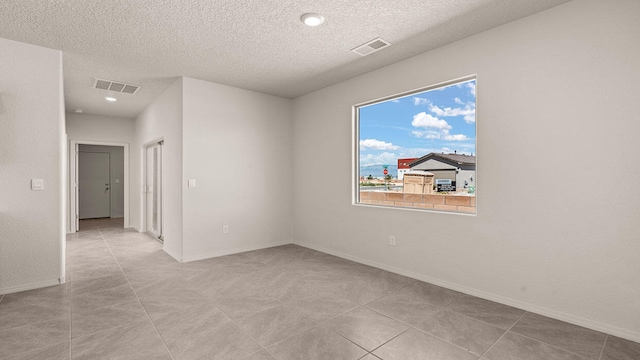 spare room featuring visible vents, a textured ceiling, and baseboards