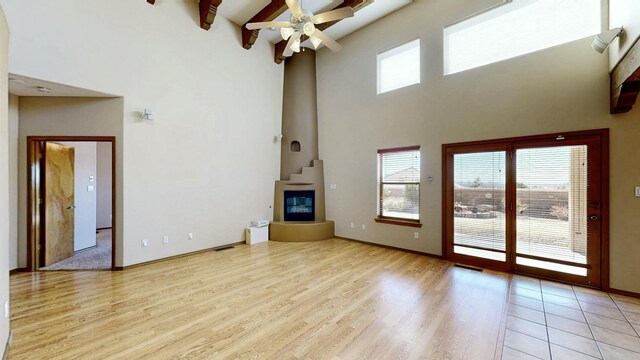 unfurnished living room with a ceiling fan, a fireplace, a towering ceiling, and light wood finished floors