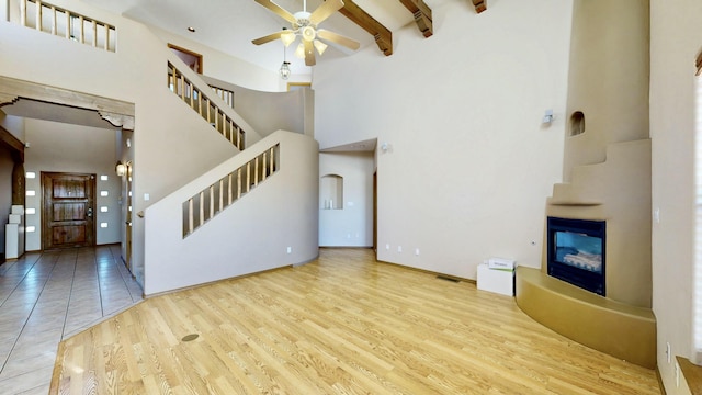 unfurnished living room featuring a glass covered fireplace, a towering ceiling, wood finished floors, stairs, and beam ceiling