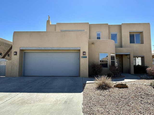 pueblo-style home with driveway, a garage, and stucco siding