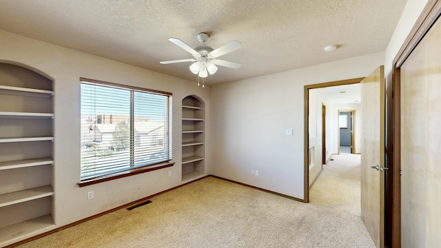 spare room with a textured ceiling, built in shelves, and light carpet