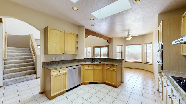 kitchen with stainless steel appliances, a peninsula, a skylight, a sink, and light brown cabinetry