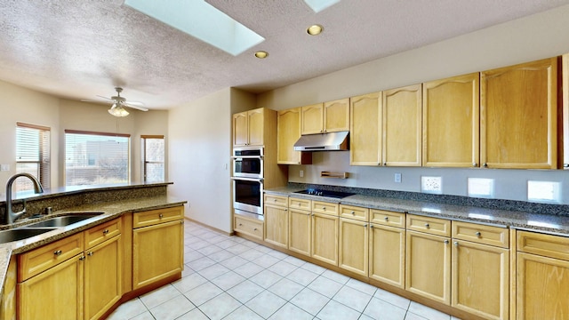 kitchen with a skylight, black electric stovetop, light brown cabinetry, a sink, and under cabinet range hood