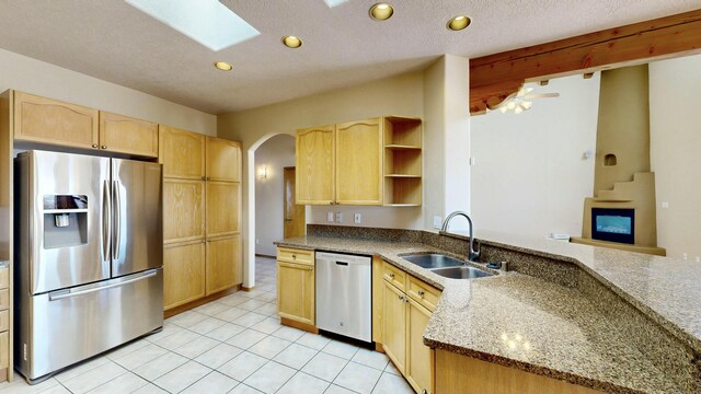 kitchen featuring appliances with stainless steel finishes, arched walkways, a sink, and light brown cabinetry