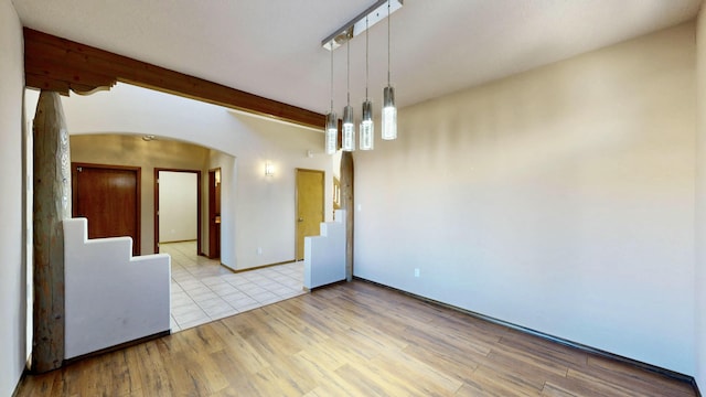 empty room with light wood finished floors, stairs, arched walkways, and beam ceiling