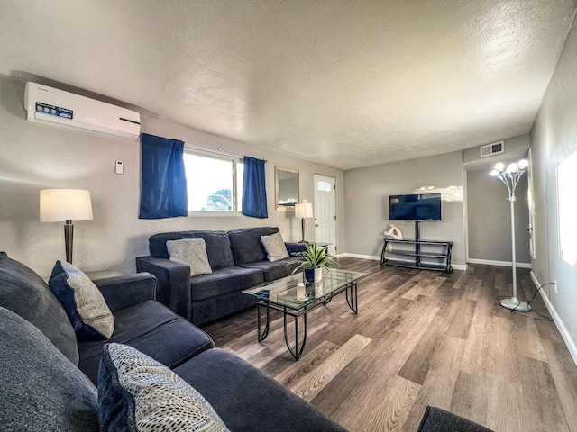 living area featuring a wall unit AC, visible vents, a textured ceiling, wood finished floors, and baseboards