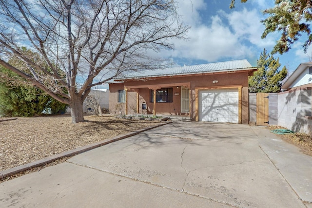 view of front facade with a garage, driveway, metal roof, fence, and stucco siding