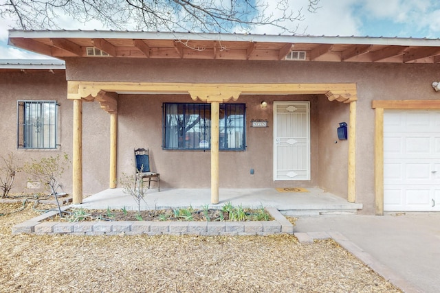 view of exterior entry featuring a porch, a garage, and stucco siding