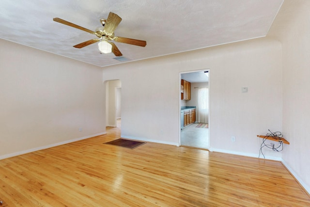 empty room with arched walkways, visible vents, light wood-style flooring, ceiling fan, and baseboards