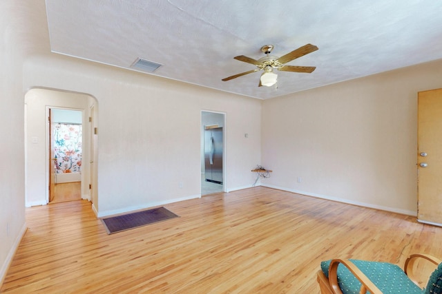 unfurnished room with arched walkways, ceiling fan, wood finished floors, visible vents, and baseboards