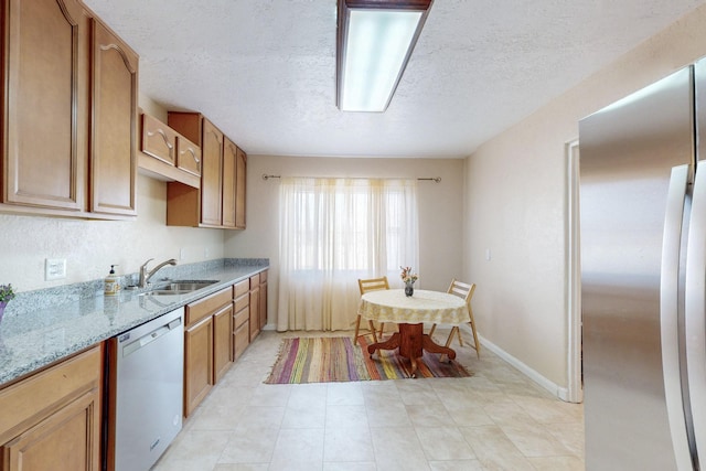 kitchen with light stone counters, stainless steel appliances, a sink, a textured ceiling, and baseboards