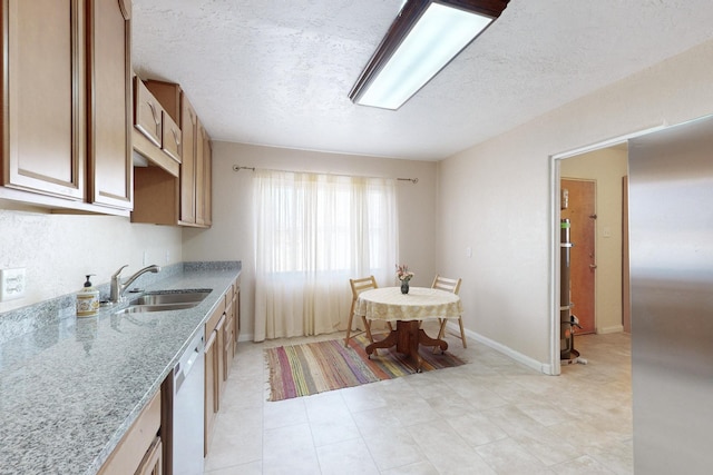 kitchen featuring light stone counters, a sink, a textured ceiling, dishwasher, and baseboards