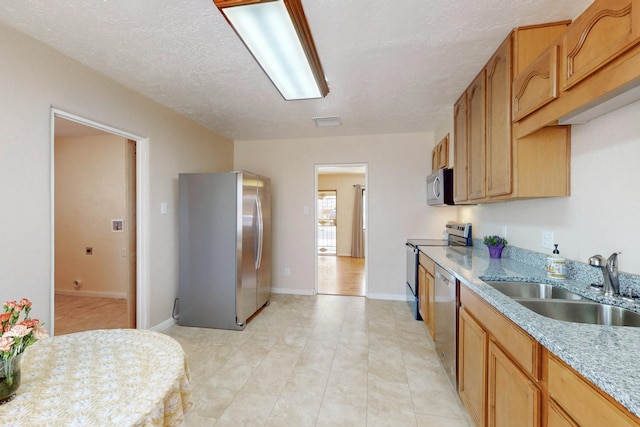 kitchen featuring baseboards, appliances with stainless steel finishes, light stone countertops, a textured ceiling, and a sink