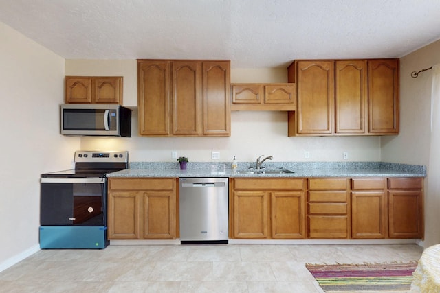 kitchen featuring appliances with stainless steel finishes, brown cabinets, a sink, and light stone countertops