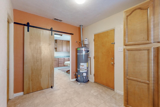 hallway with a barn door, secured water heater, visible vents, and baseboards