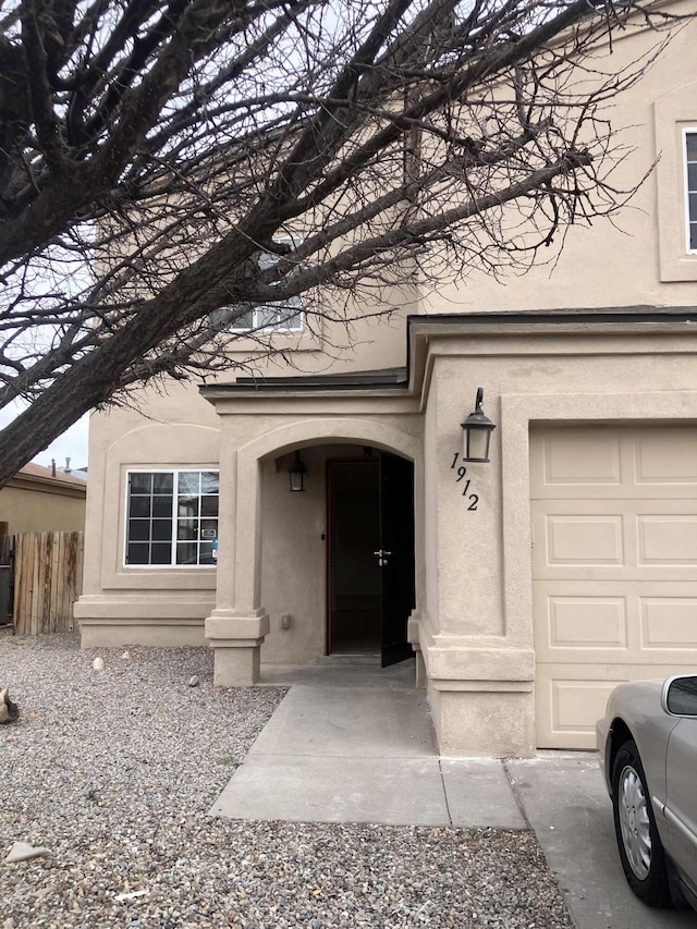 doorway to property with a garage, fence, and stucco siding