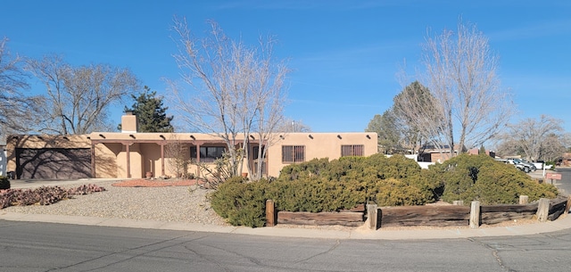 pueblo-style house with a garage, a chimney, concrete driveway, and stucco siding