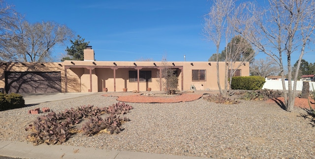 pueblo-style home with a chimney, fence, and stucco siding