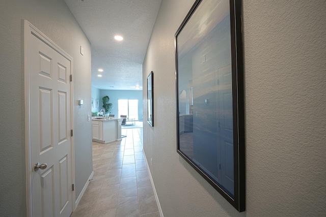 hall featuring light tile patterned floors, baseboards, a textured wall, a textured ceiling, and recessed lighting