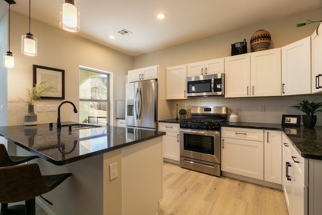 kitchen featuring visible vents, appliances with stainless steel finishes, a sink, light wood-type flooring, and backsplash