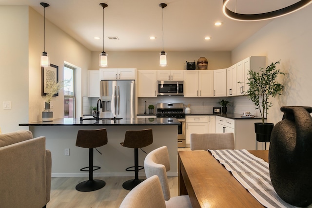 kitchen featuring a breakfast bar area, appliances with stainless steel finishes, light wood finished floors, dark countertops, and tasteful backsplash