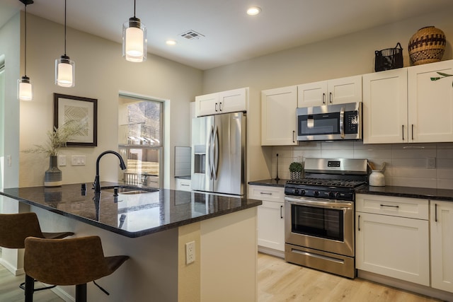 kitchen featuring light wood finished floors, visible vents, decorative backsplash, appliances with stainless steel finishes, and a sink