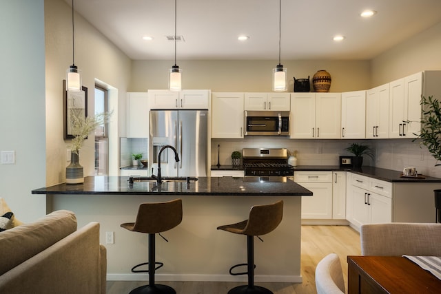 kitchen featuring stainless steel appliances, decorative backsplash, a sink, light wood-type flooring, and a peninsula