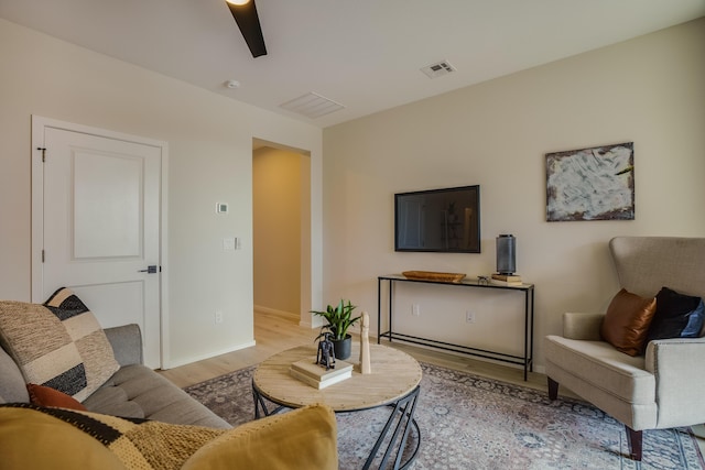 living room with light wood-type flooring, baseboards, visible vents, and a ceiling fan