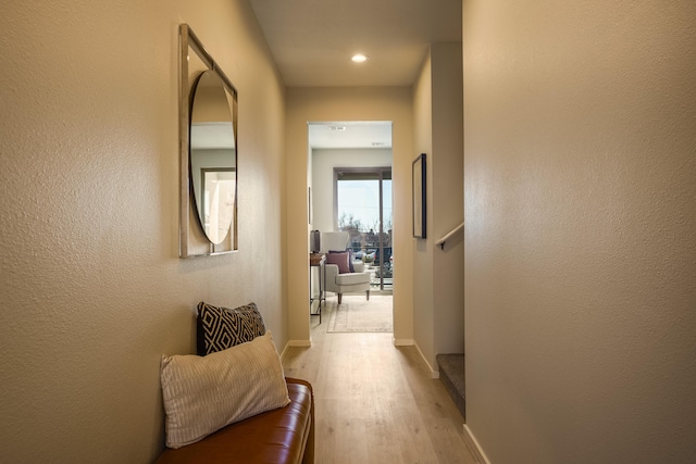 corridor featuring a textured wall, wood finished floors, and baseboards