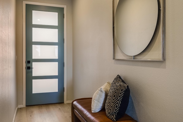 doorway with baseboards, wood finished floors, and a textured wall