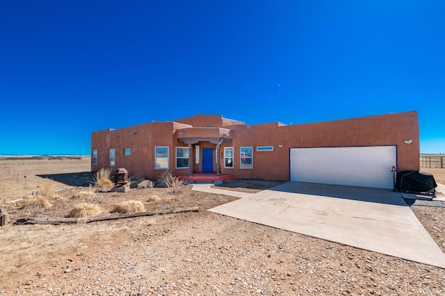 pueblo-style home with a garage, concrete driveway, and stucco siding