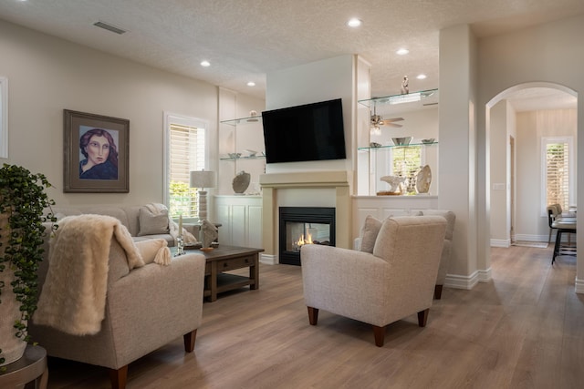 living room featuring visible vents, a textured ceiling, a glass covered fireplace, arched walkways, and light wood finished floors