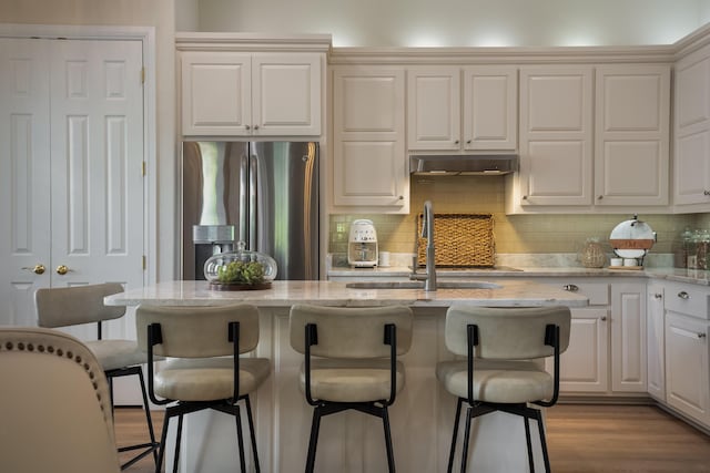 kitchen with under cabinet range hood, decorative backsplash, stainless steel fridge, and a kitchen bar