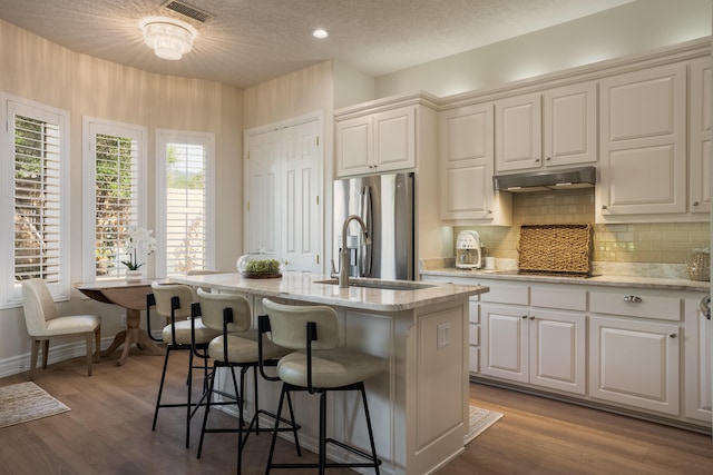 kitchen featuring under cabinet range hood, appliances with stainless steel finishes, a kitchen breakfast bar, and wood finished floors