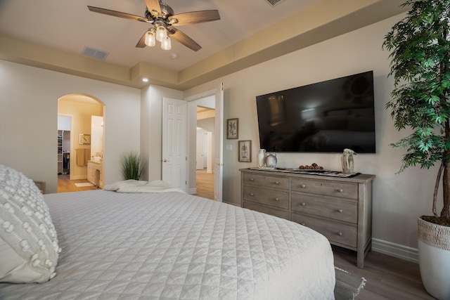 bedroom featuring a ceiling fan, wood finished floors, visible vents, baseboards, and arched walkways