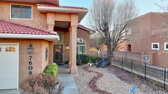 property entrance featuring a tiled roof, fence, and stucco siding