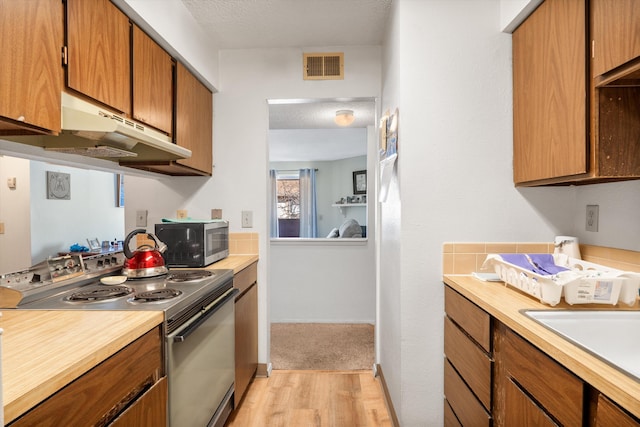 kitchen featuring under cabinet range hood, range with electric stovetop, visible vents, light countertops, and stainless steel microwave