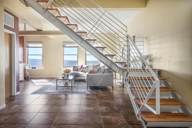 tiled living room with a high ceiling, visible vents, baseboards, and stairs