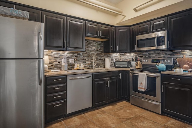 kitchen featuring stainless steel appliances, dark cabinets, a sink, and backsplash