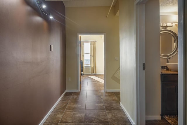 corridor featuring dark tile patterned flooring, a sink, and baseboards