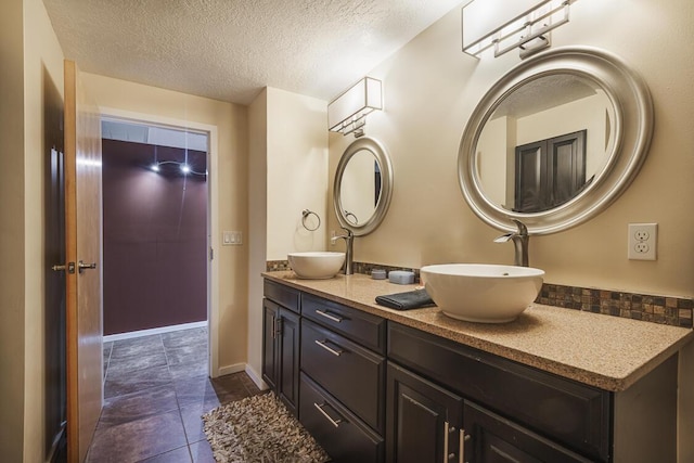 full bath featuring a textured ceiling, double vanity, a sink, and baseboards