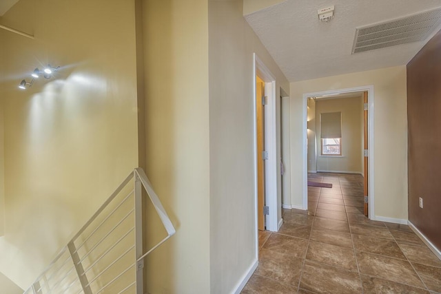 corridor with a textured ceiling, tile patterned flooring, an upstairs landing, visible vents, and baseboards