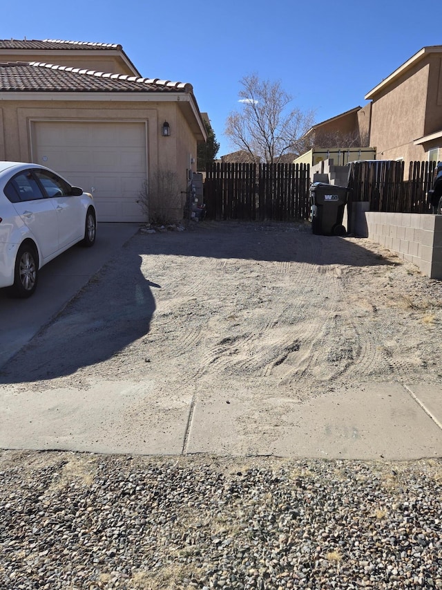 exterior space featuring an attached garage, a tile roof, fence, and stucco siding