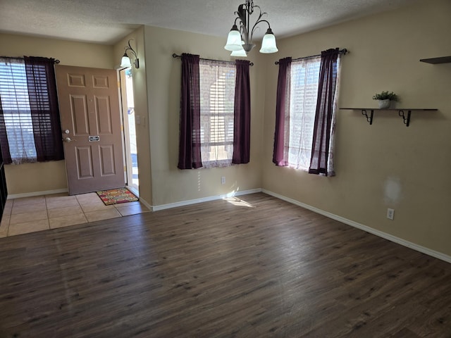 foyer entrance featuring a notable chandelier, baseboards, a textured ceiling, and wood finished floors